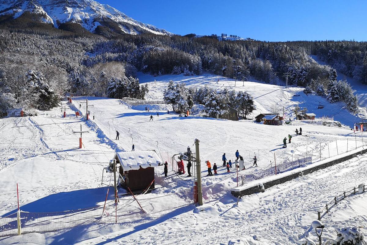 A snowy ski slope with a mountain backdrop, ski lifts, and a small lodge.