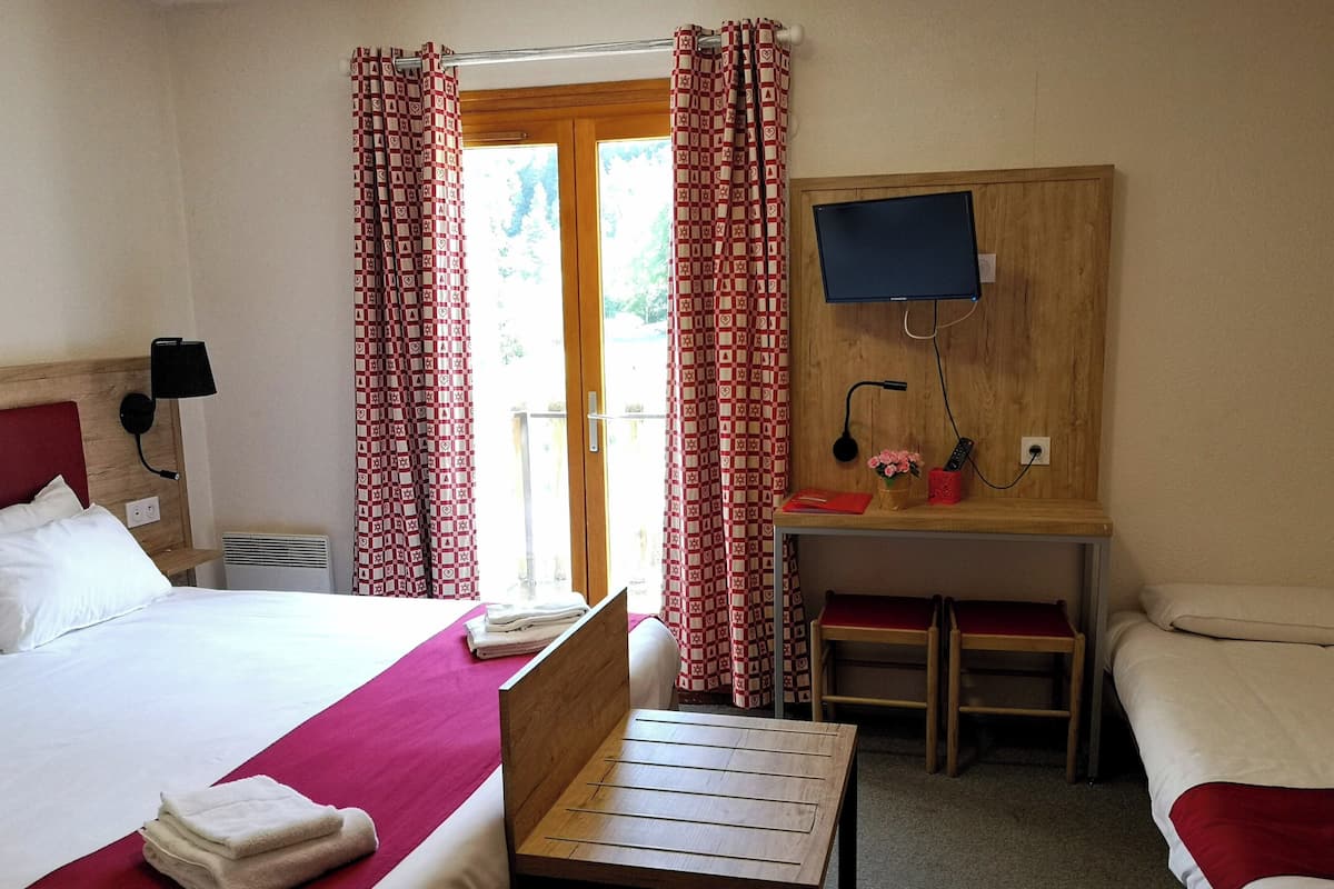 A hotel room with a bed, a desk, a chair, a TV, and a window with curtains.