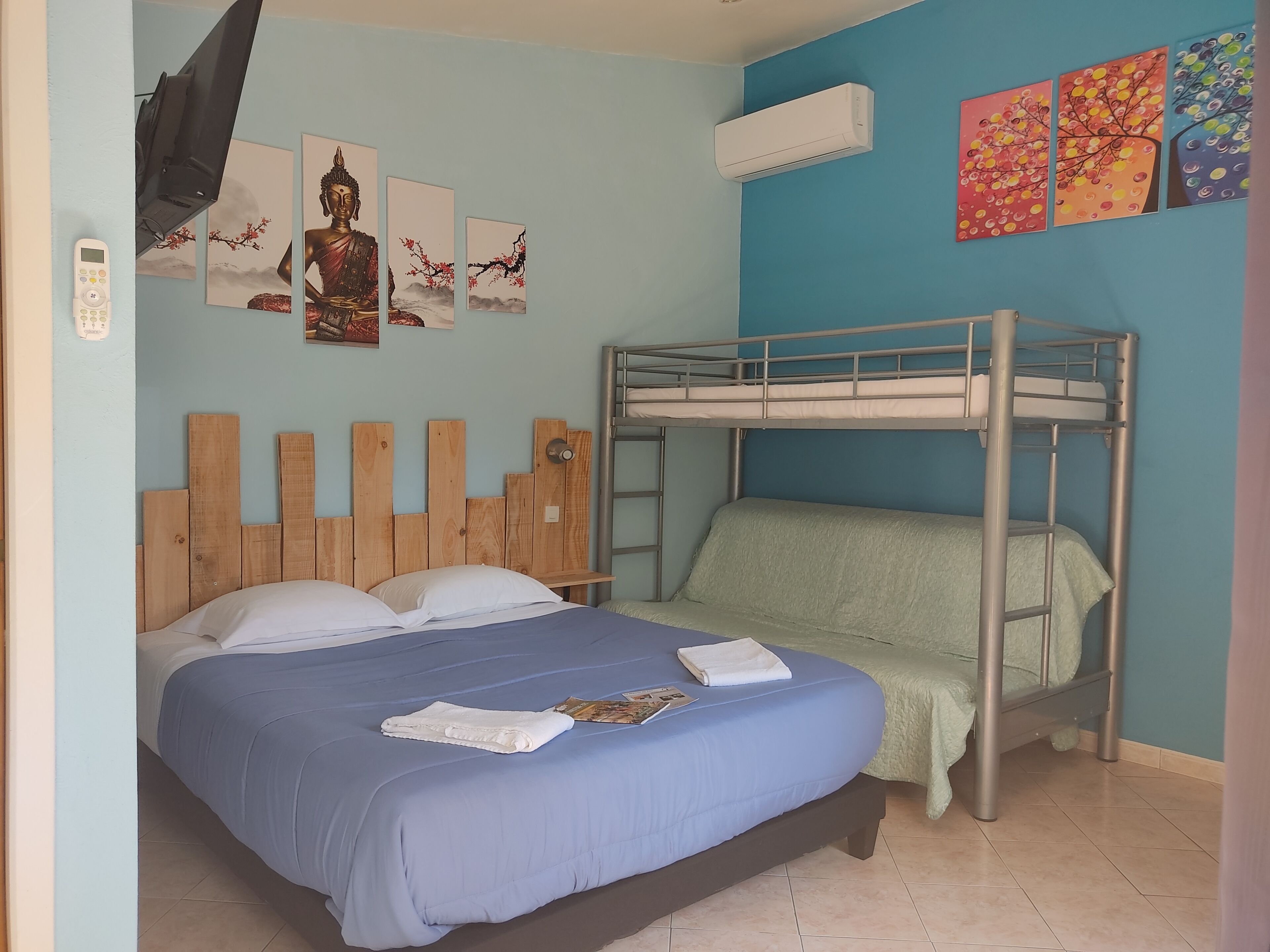 Un dormitorio con una cama litera, cabecera de madera, colcha azul y aire acondicionado instalado en la pared.