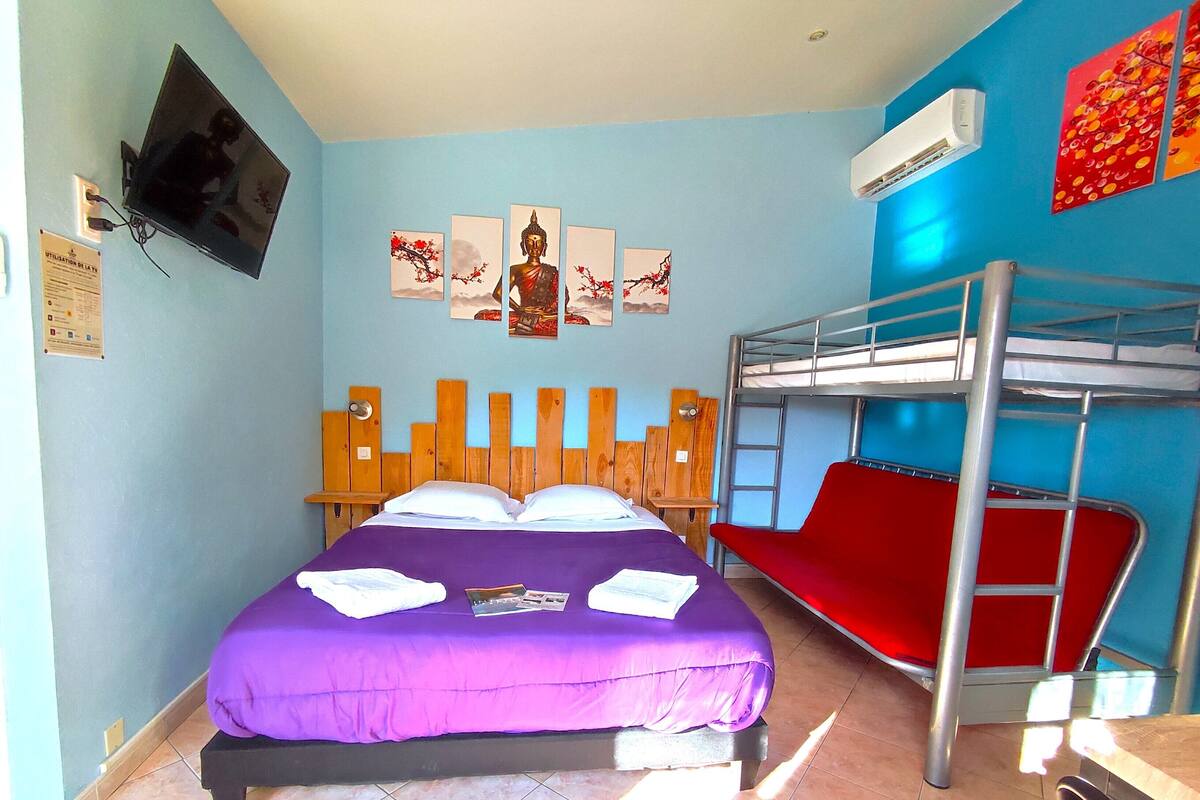 A room with a bunk bed, a single bed with a purple bedspread, a red chair, and wall art.