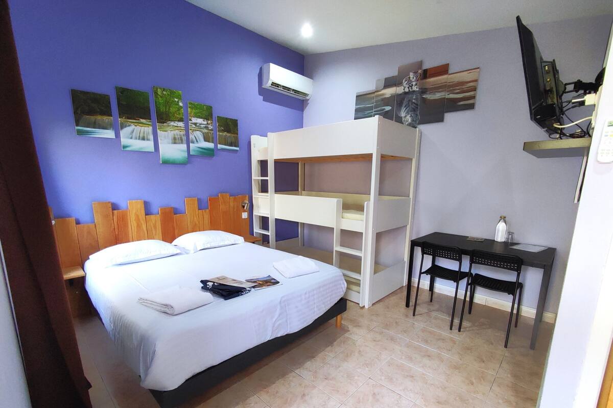 A room with a bed, bunk beds, a desk, and a TV.