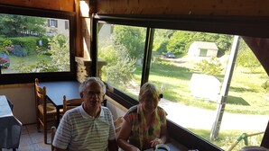 A dining area with a table set for two, a window view of a garden, and a rustic interior with wooden beams. - La Maison de Tari (Vitrac)