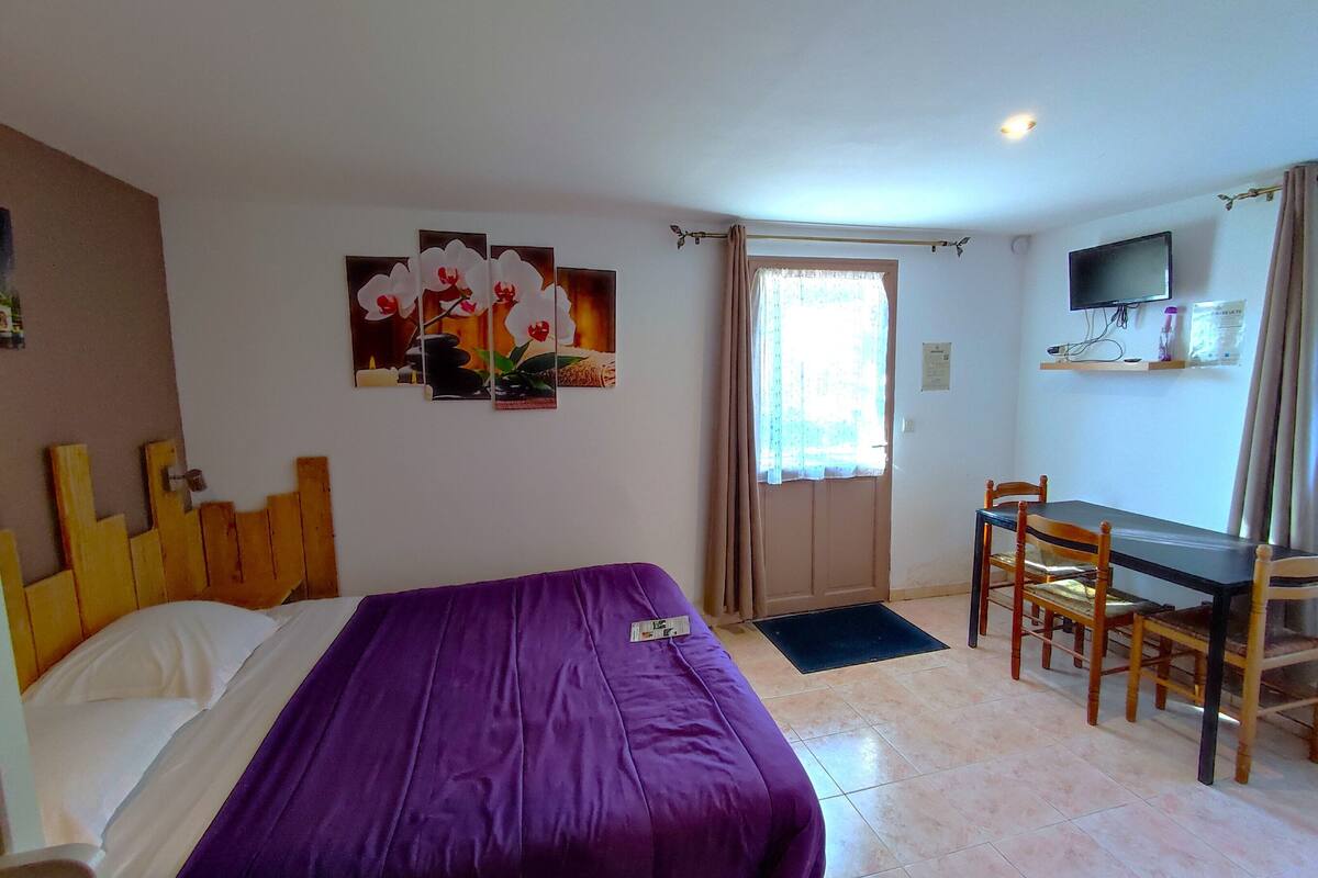 A hotel room with a bed, a desk, a chair, a TV, and artwork on the wall.