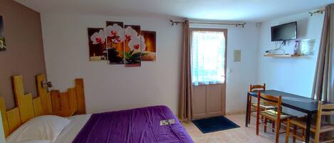 Una habitación de hotel con cama, escritorio, silla, televisor y obras de arte en la pared.