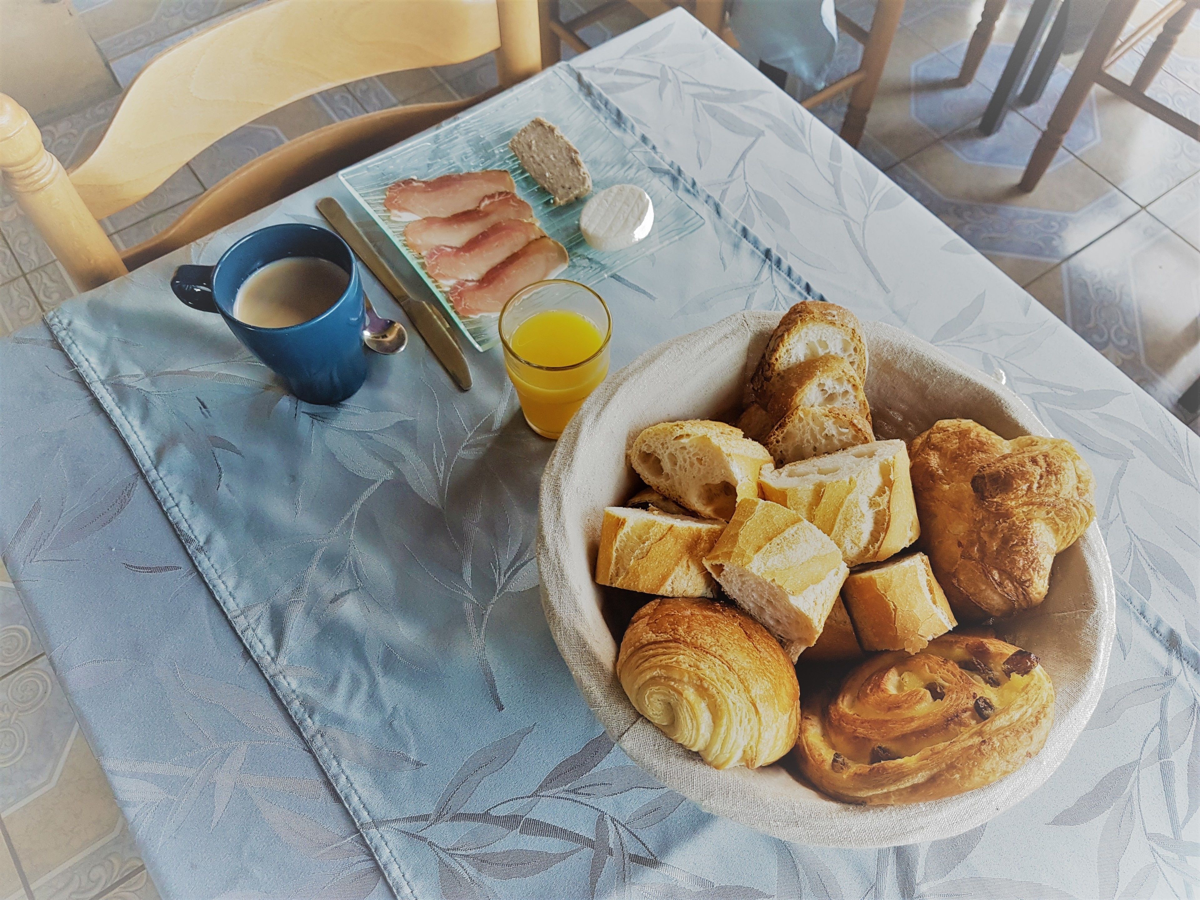 A breakfast table with croissants, bread, a cup of coffee, and a glass of orange juice.
