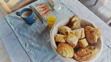 A breakfast table with croissants, bread, a cup of coffee, and a glass of orange juice.