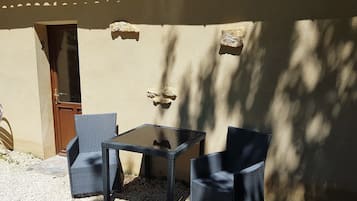 Un espacio al aire libre con dos sillas, una mesa, una puerta y un muro con textura.