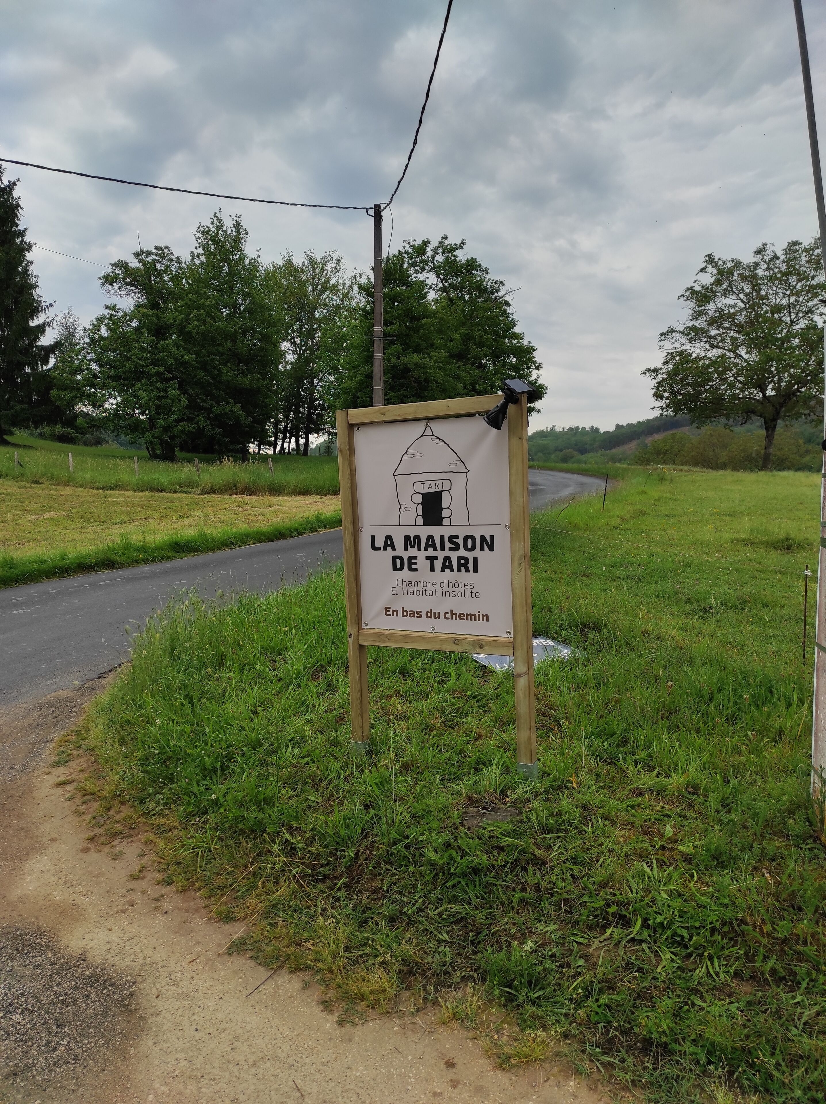 Un cartel para 'LA MAISON DE TARI' que indica un hotel y una casa de huéspedes con un diseño rústico de estilo campestre.