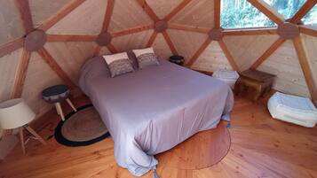 Un interior de madera cálido y circular, con una cama, almohadas, un taburete pequeño y una lámpara.
