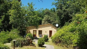 A small, single-story building surrounded by dense greenery, with a paved path leading to the entrance. - La Maison de Tari (Vitrac)
