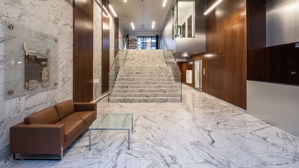 A modern lobby with marble flooring, a glass coffee table, a brown sofa, and a staircase leading to another floor. - Good Time Apartment (Warsaw)