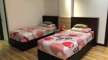 Habitación de hotel con dos camas individuales, piso de madera, unidad de aire acondicionado, mesita de noche con un florero y un espejo en la pared.