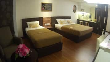 A hotel room with two single beds, a small desk, a chair, and a flower vase.