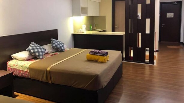 A hotel room with a bed, a bedside table, a small desk with a chair, a kitchenette, and a bathroom door.