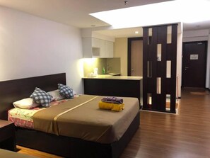Ein Hotelzimmer mit Bett, Nachttisch, kleinem Schreibtisch mit Stuhl, Küchenzeile und Badtür.