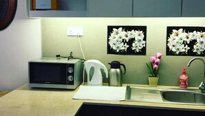 A kitchen with a microwave, kettle, sink, and decorative flowers on the wall.