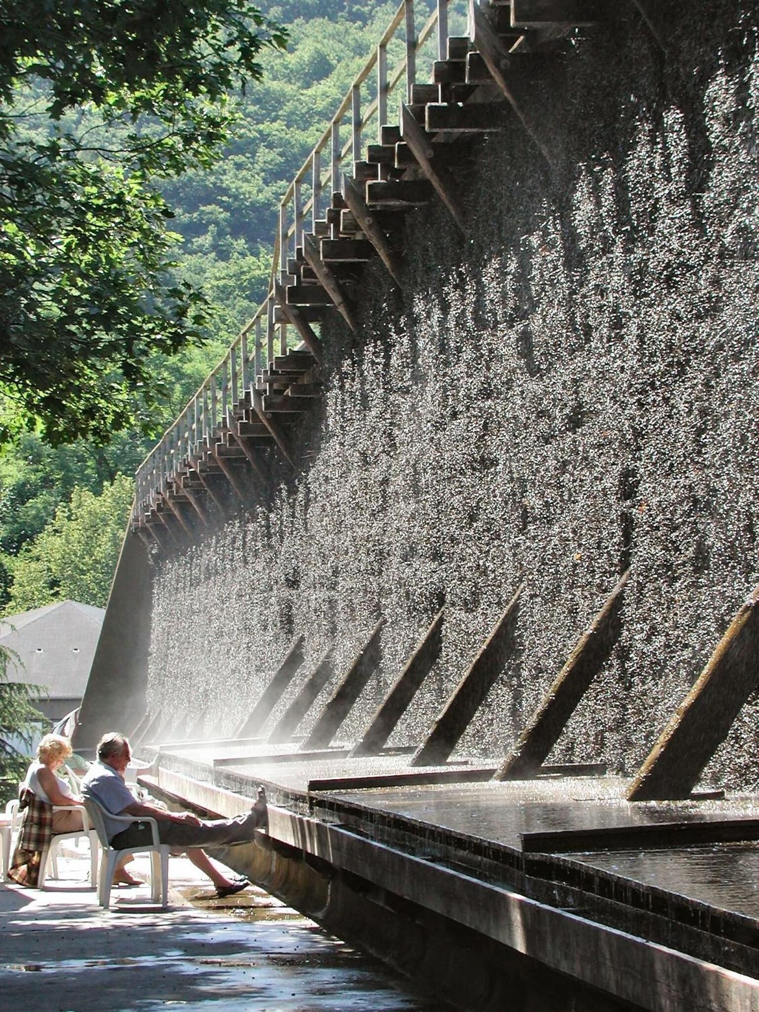 A water feature with a cascading waterfall, a staircase, and a seating area with people.