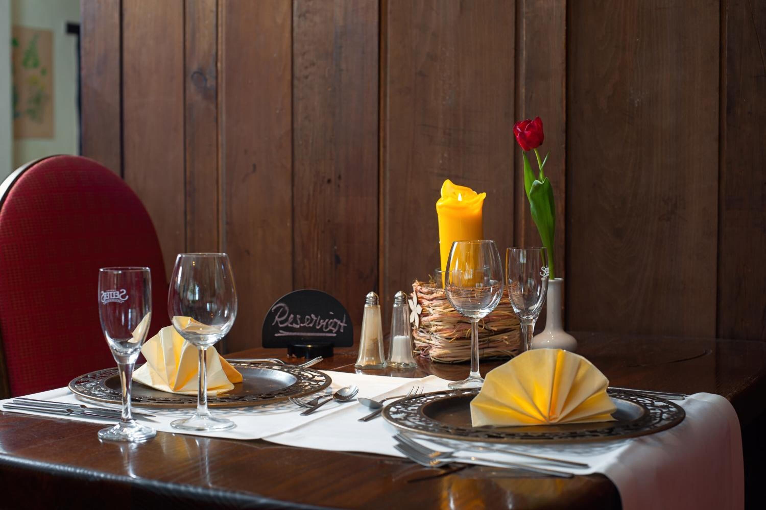 Een eettafel gedekt met wijnglazen, borden en een kaars.
