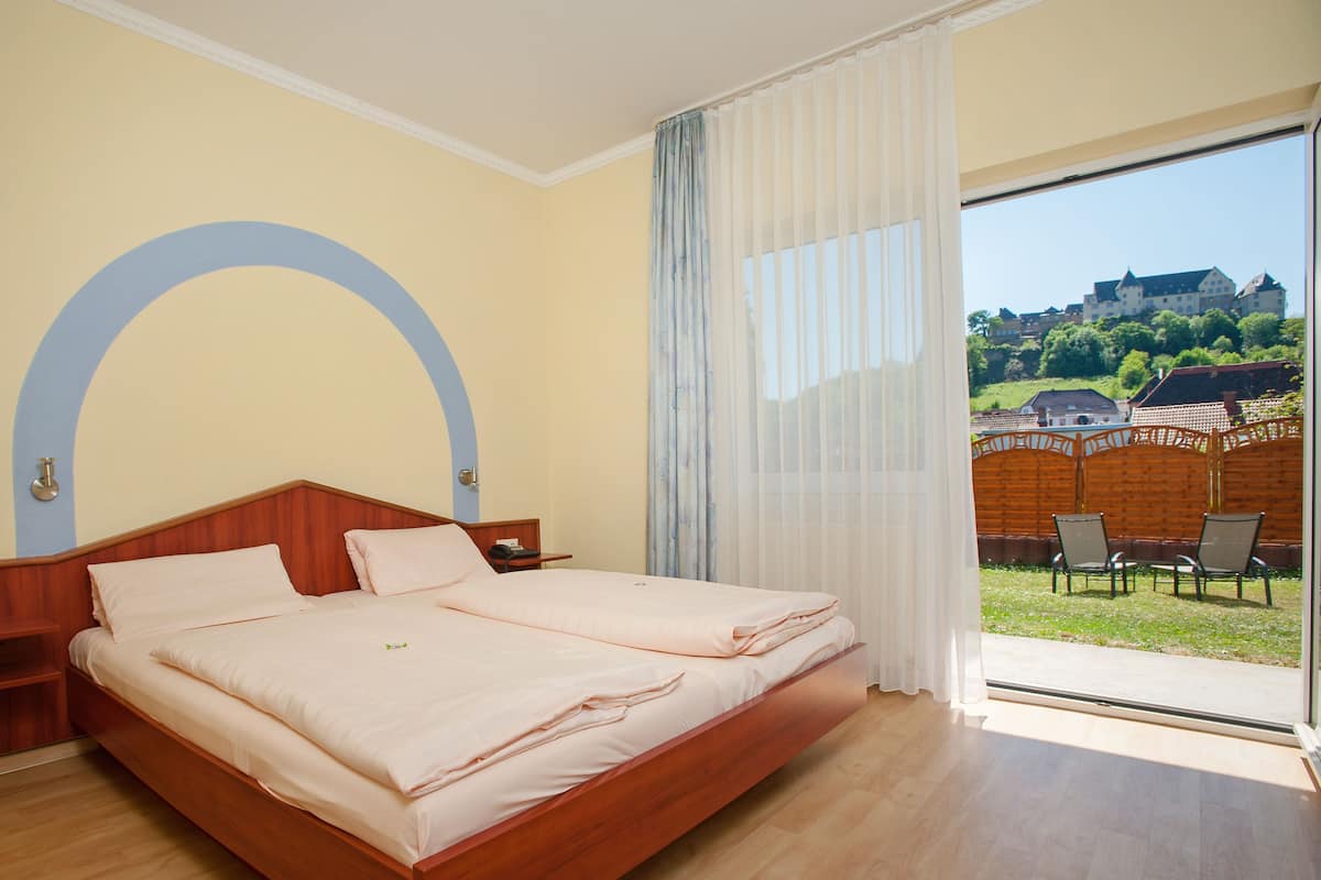 A double bed with a wooden headboard, a nightstand, and a large window with sheer curtains.