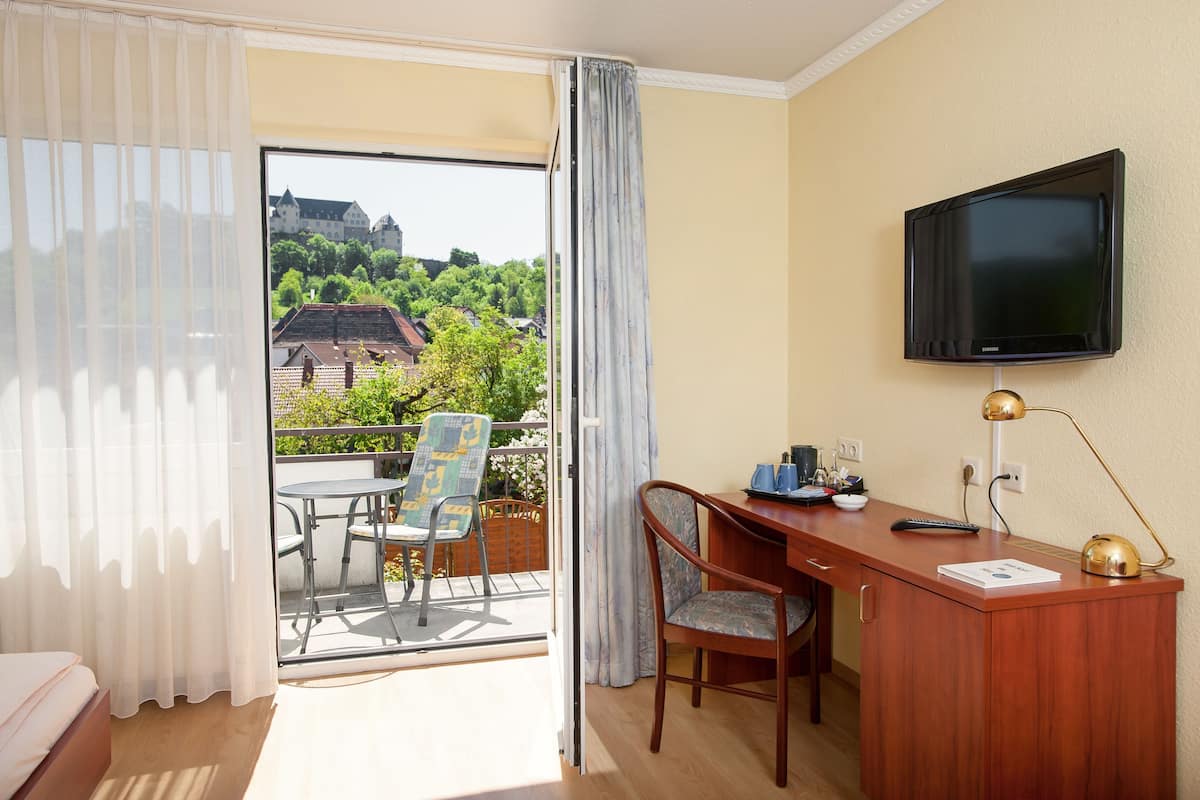 A hotel room with a balcony, a desk, a chair, a TV, and a bed.