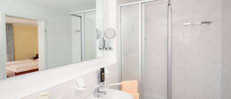 Un baño con lavamanos blanco, espejo, secador de pelo y cabina de ducha de vidrio.