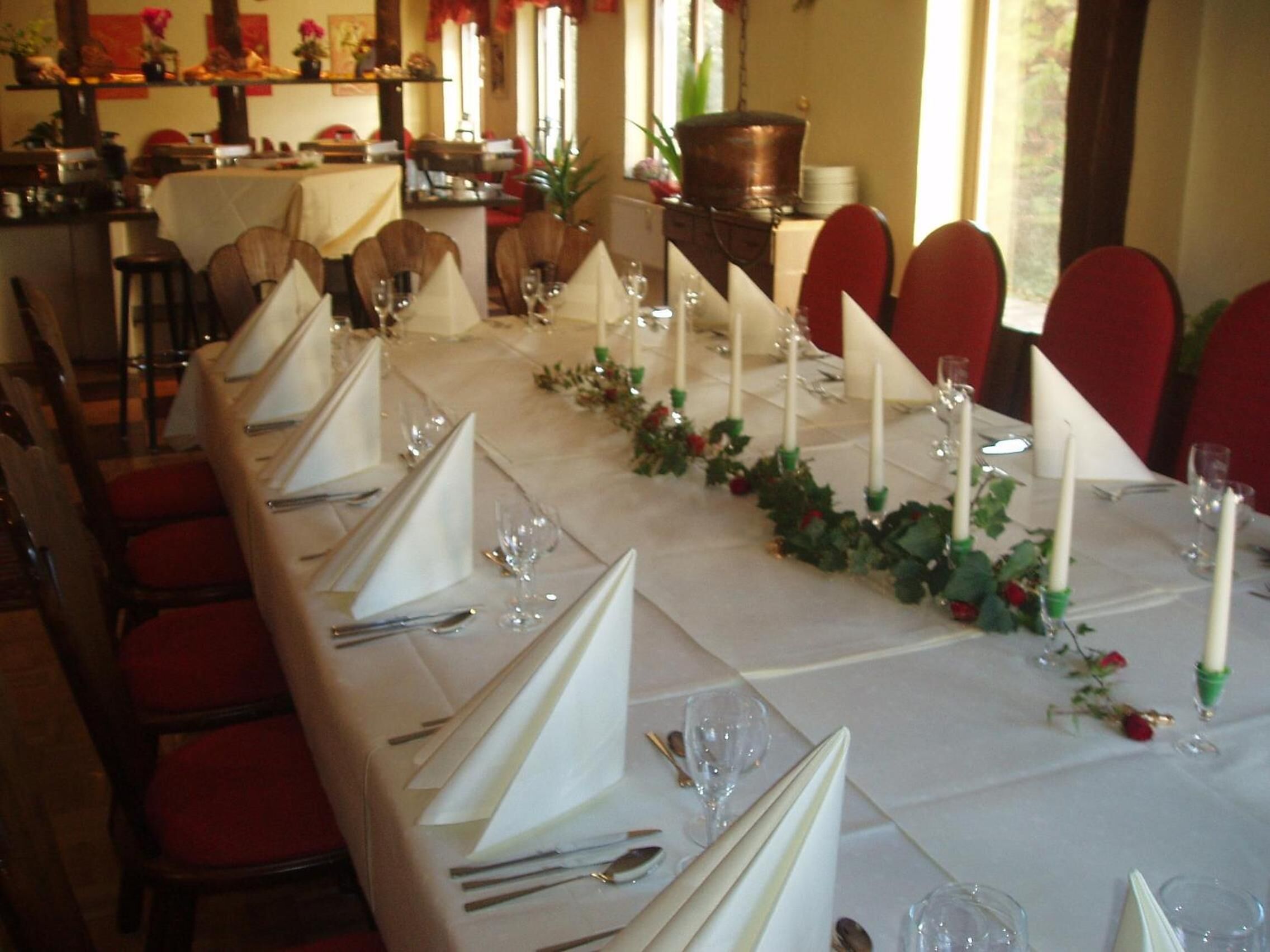 A long dining table set with white napkins, silverware, and wine glasses, surrounded by red chairs.