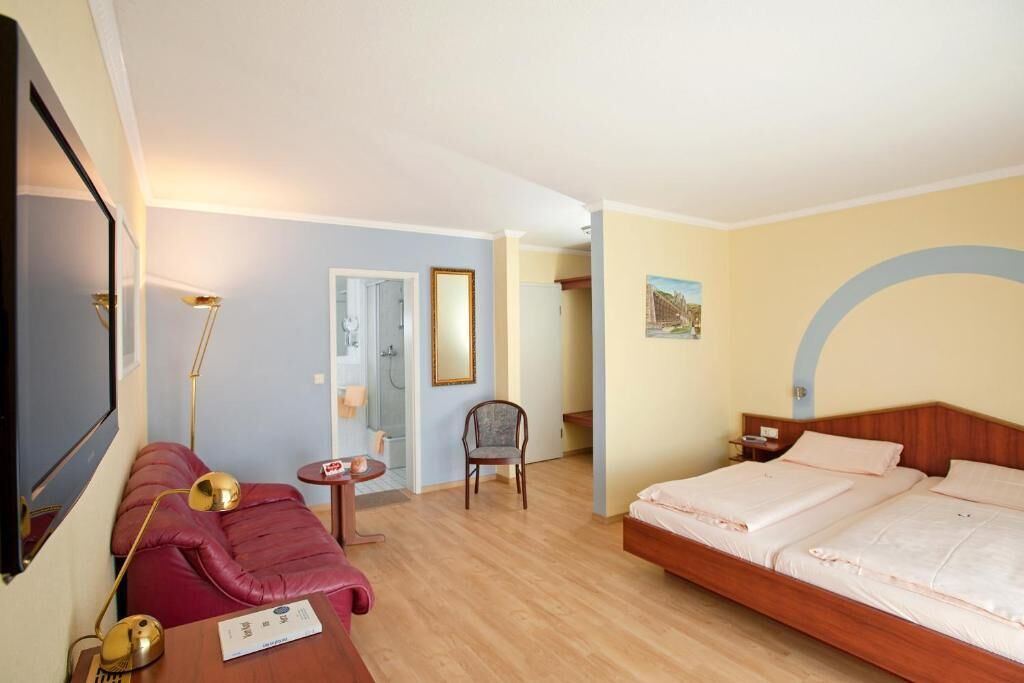 A hotel room with a bed, a sofa, a chair, a small table, and a mirror.