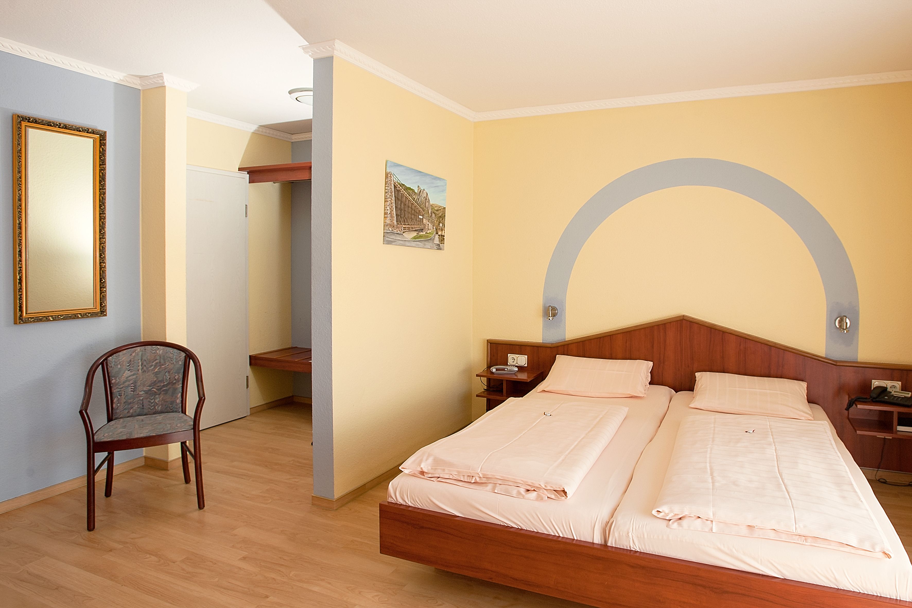 Ein Schlafzimmer mit einem Holzbett, einem Sessel, einem Nachttisch und einem Spiegel an der Wand.
