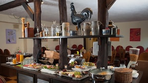 Montaje de bufé con diferentes alimentos y bebidas, vigas de madera y un gallo decorativo.