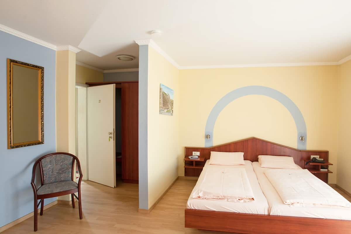 A hotel room with a wooden bed, a chair, a mirror, and a door leading to another room.