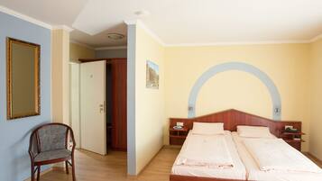 Una camera d'albergo con un letto di legno, una sedia, uno specchio e una porta che dà su un'altra stanza.