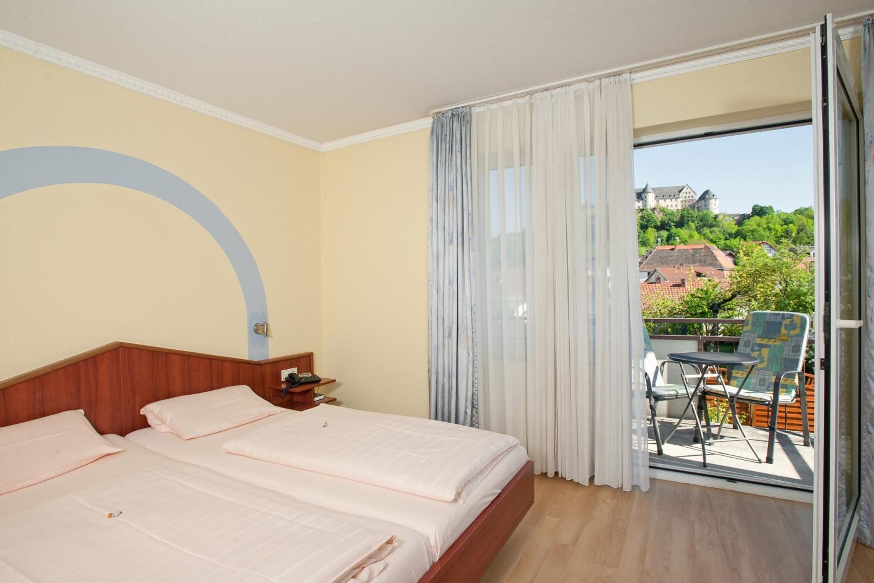 Habitación de hotel con dos camas, cabecera de madera, una mesita con una silla y un balcón con mesa y sillas.