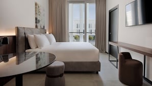 Une chambre d’hôtel moderne dotée d’un grand lit, d’une télévision à écran plat, d’un bureau et offrant une vue sur la ville grâce à de grandes fenêtres.
