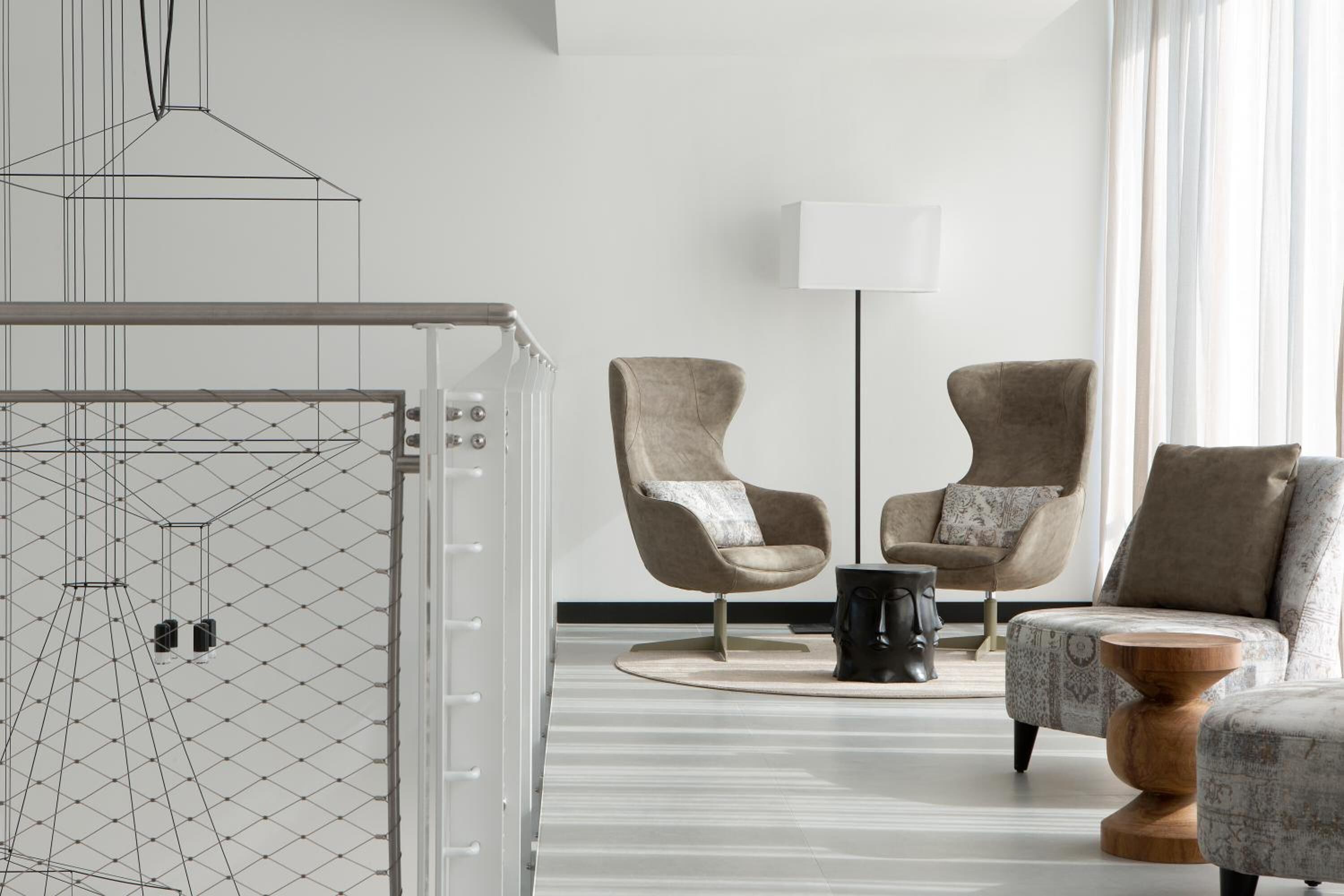 A modern living room with a geometric light fixture, two armchairs, a floor lamp, and a patterned rug.