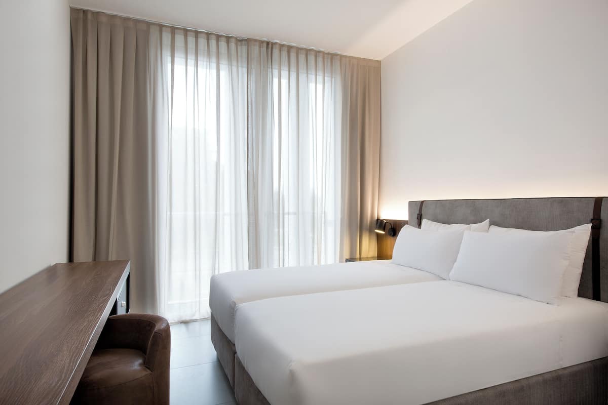 A hotel room with a large bed, a desk, and a window with curtains.