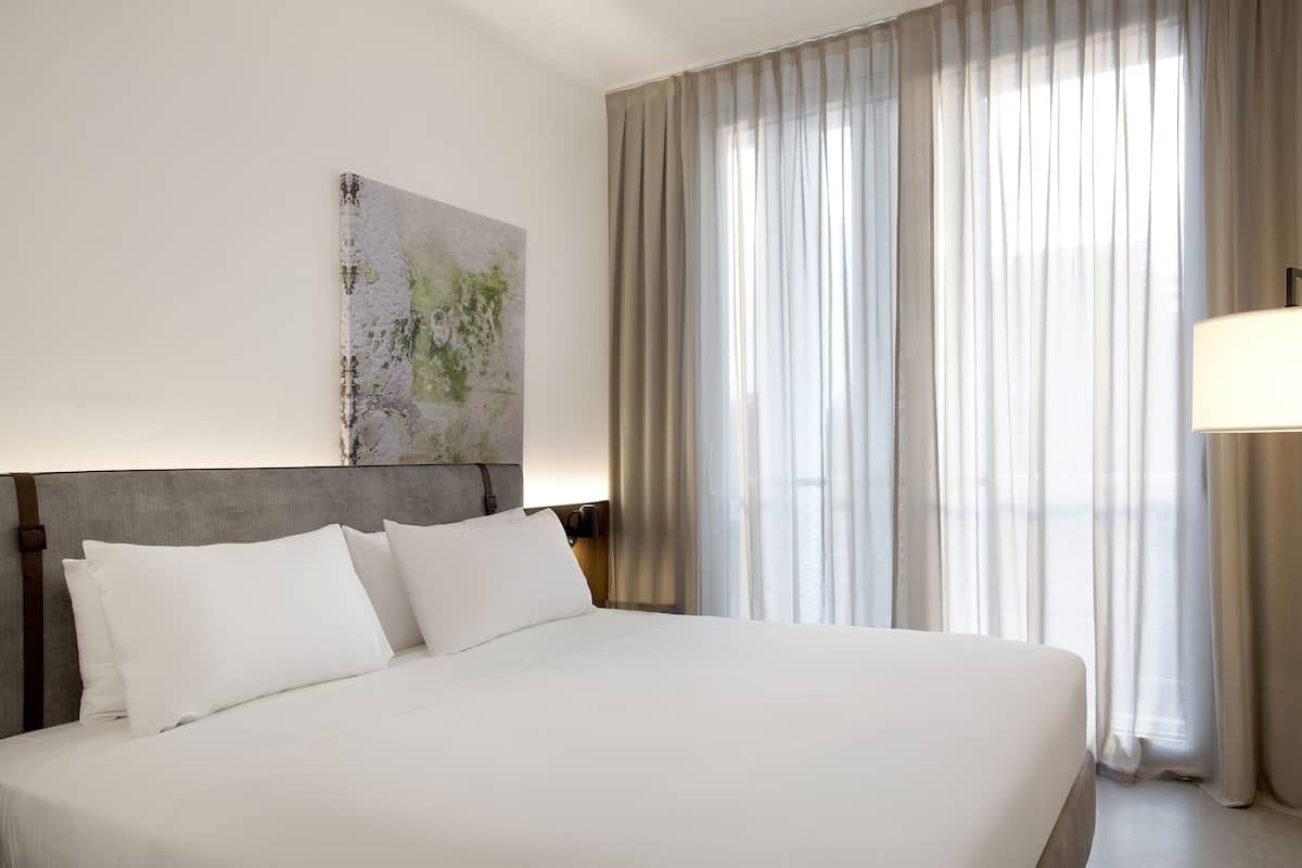 A large bed with white linens, a headboard, and a bedside lamp.