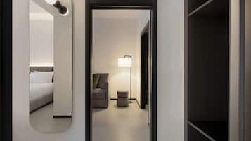 A modern hotel room with a large mirror, a bed, a sofa, a floor lamp, and a small round table.