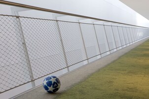 Una cerca de malla metálica con una pelota de fútbol en el suelo.