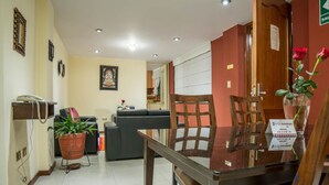 A hotel reception area with a reception desk, a telephone, a potted plant, a sofa, and a wooden chair. - Apart Hotel Incamin (Arequipa)
