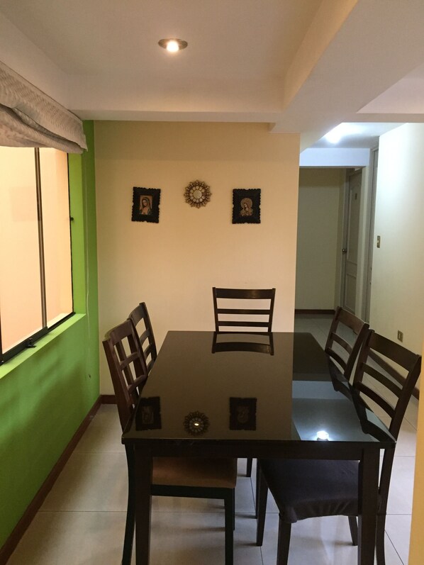 Un comedor con una mesa y cuatro sillas, una ventana con persianas y tres adornos colgados en la pared.