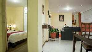 A hotel room with a bed, a desk, a chair, a potted plant, a sofa, and a dining table. - Apart Hotel Incamin (Arequipa)