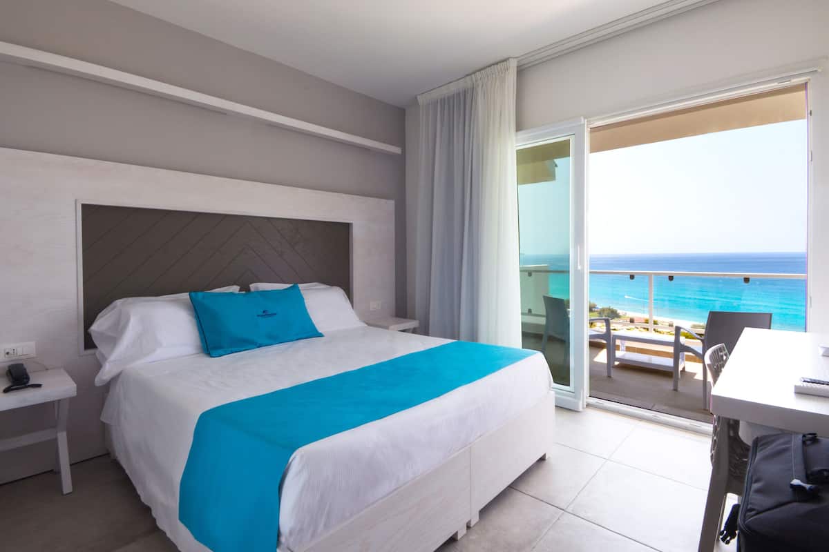 Una camera d'albergo con un letto, un comodino, una scrivania e vista sull'oceano.