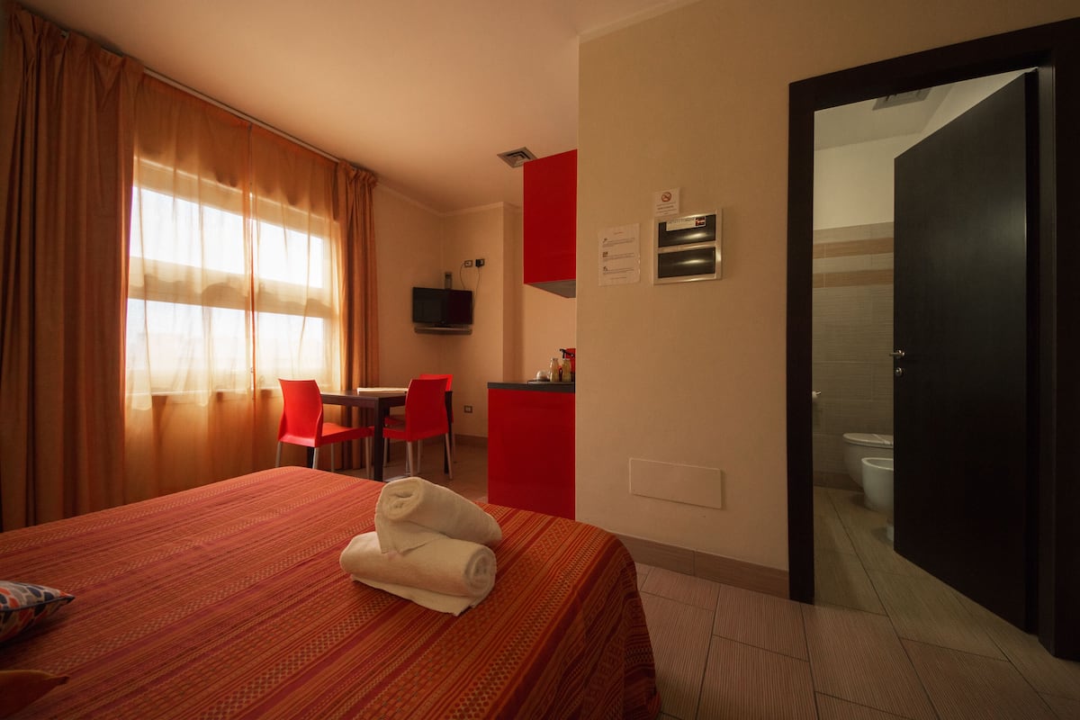 A hotel room with a bed, a desk, a chair, and a bathroom visible through an open door.