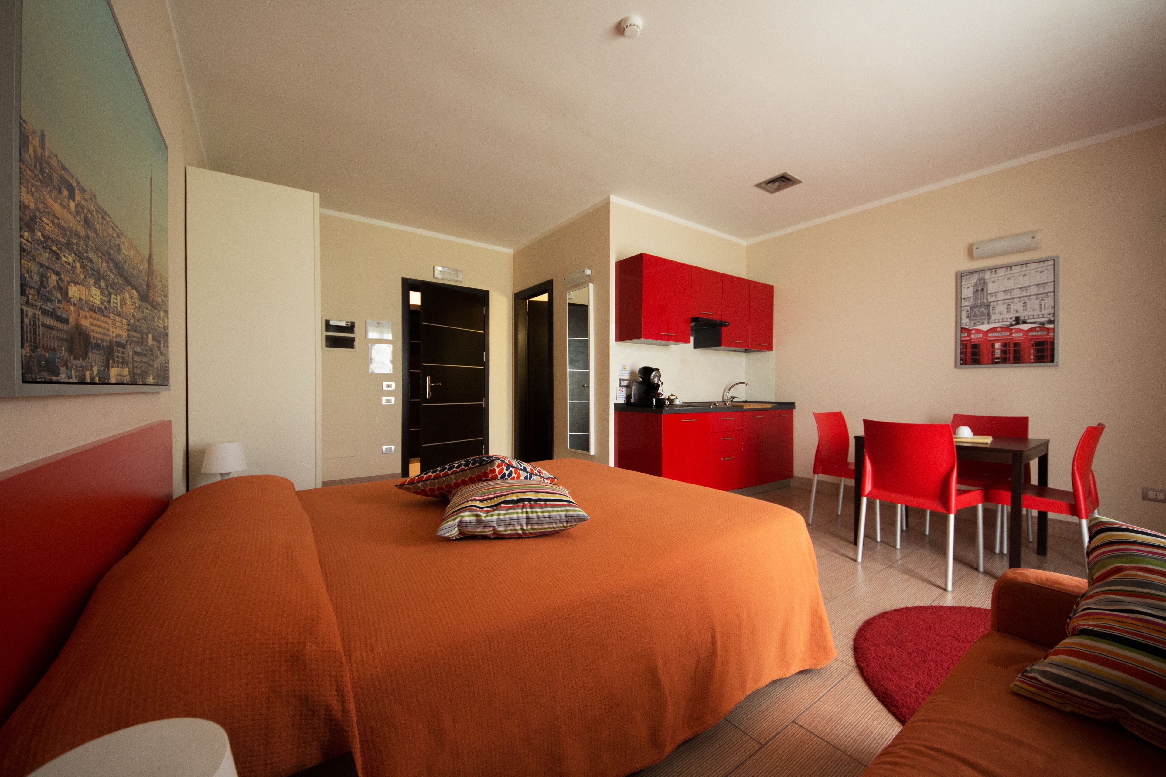 Ein Hotelzimmer mit einem großen Bett, einem roten Essbereich und einer Küchenzeile.