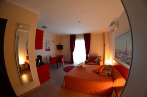 Habitación de hotel con cama, escritorio, silla, espejo y ventana con cortinas.