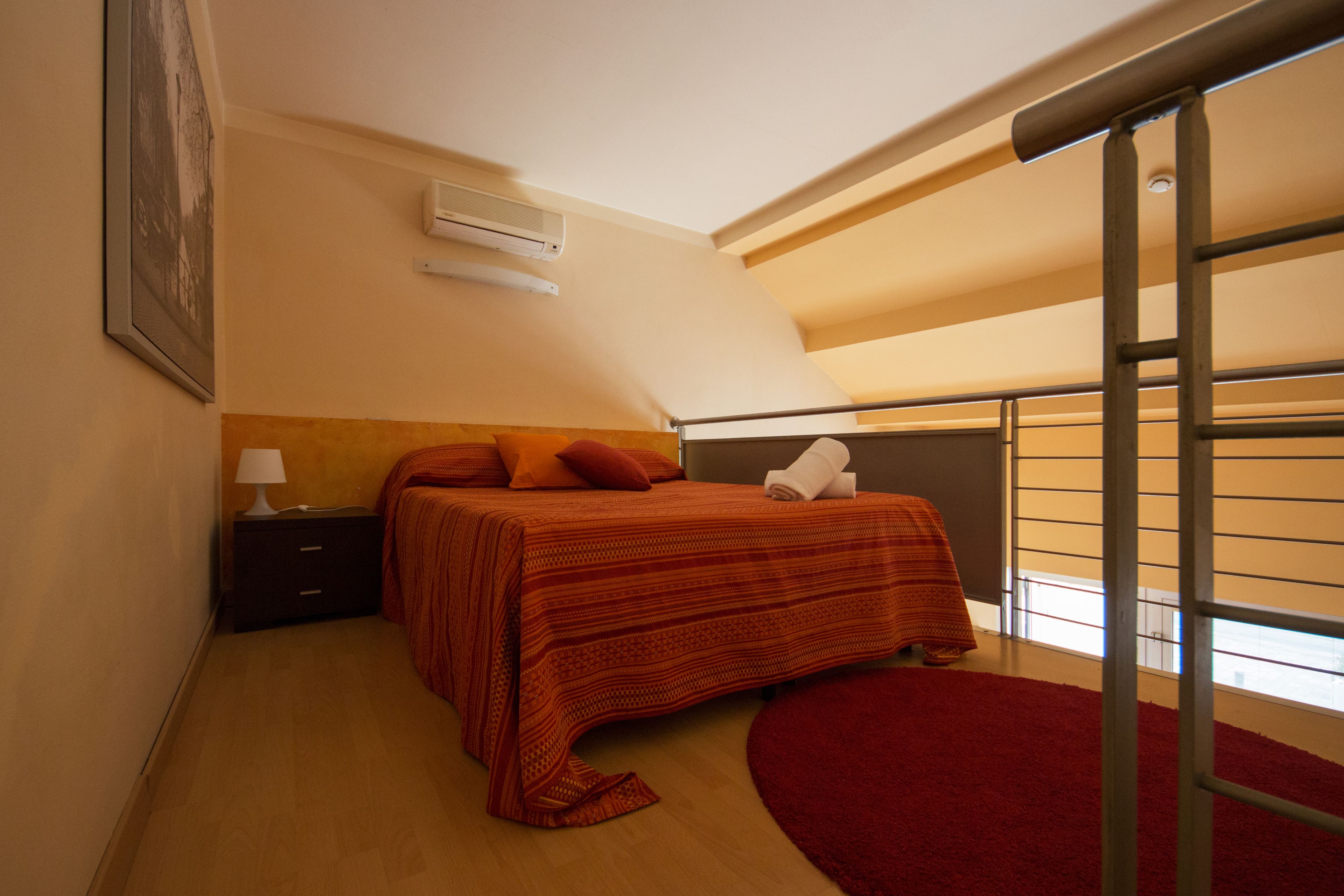 Ein Schlafzimmer mit Bett, Nachttisch, Lampe, einem roten Teppich und einem Fenster mit Blick.