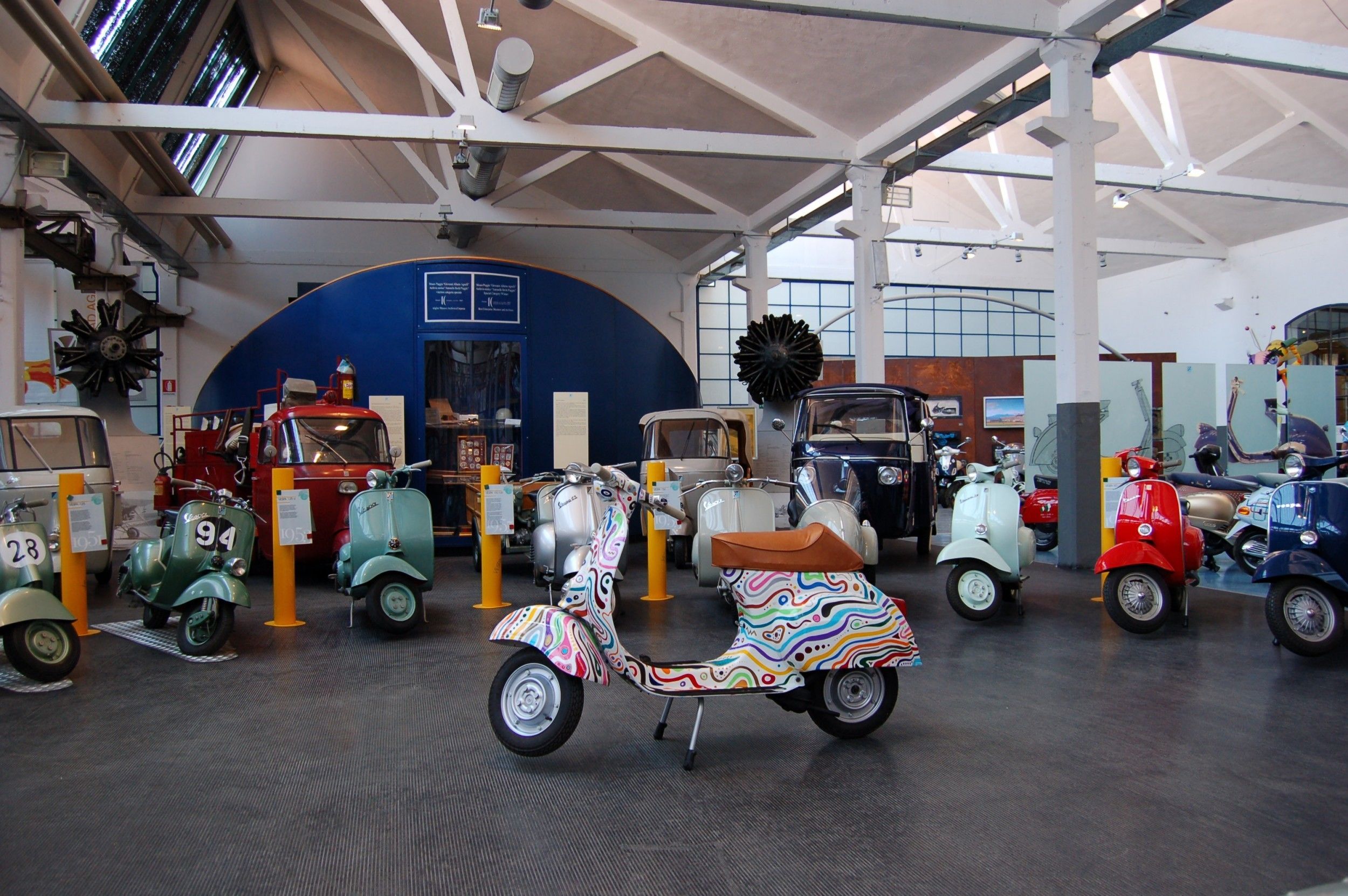 A museum with vintage scooters on display, including a colorful one in the center.