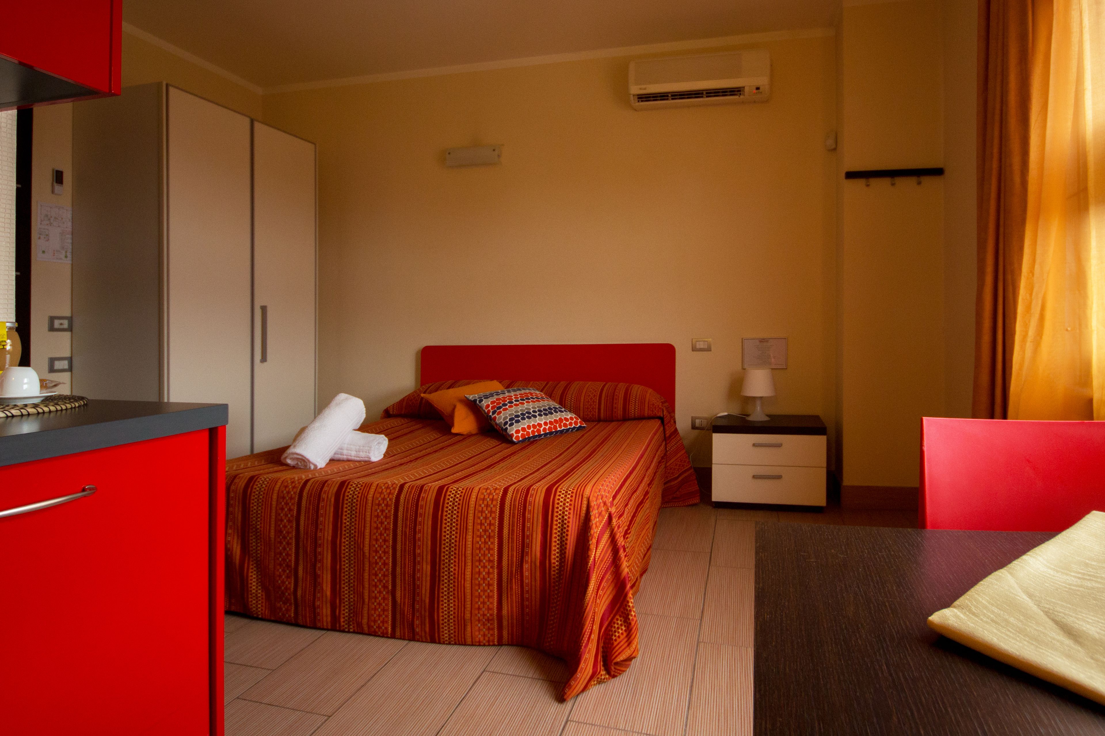 Et hotelværelse med seng, skrivebord, stol, garderobeskab og aircondition.