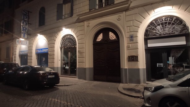 A building with a large arched entrance, a sign for 'Pilia Sport', and a parked car in front. - Double B Ferruccio I (Rome)