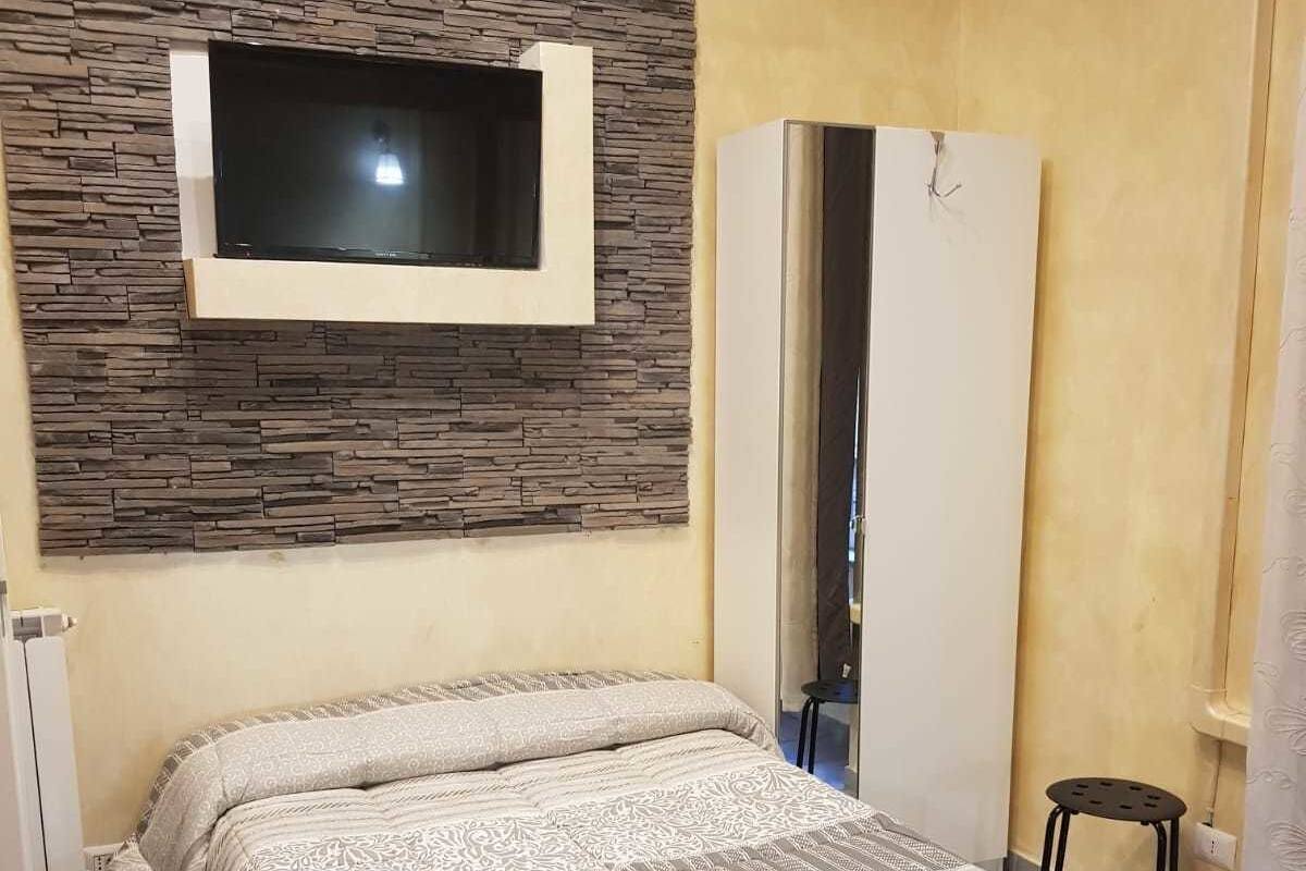 Un dormitorio con cama, armario, televisor montado en una pared de piedra y espejo.